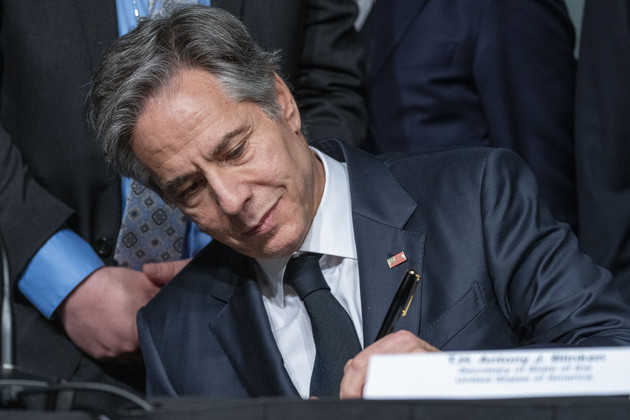 Antony Blinken signs an agreement while seated at a table.
