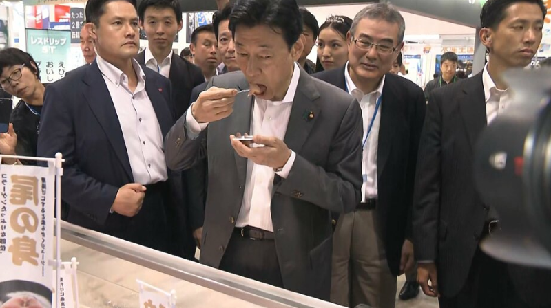 西村康稔在展览会上食用水产品，富士新闻网23日报道视频截图