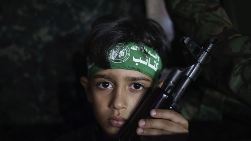 在2021年的以巴冲突，一名男孩手持武器参加哈马斯的悼念集会。 美联社