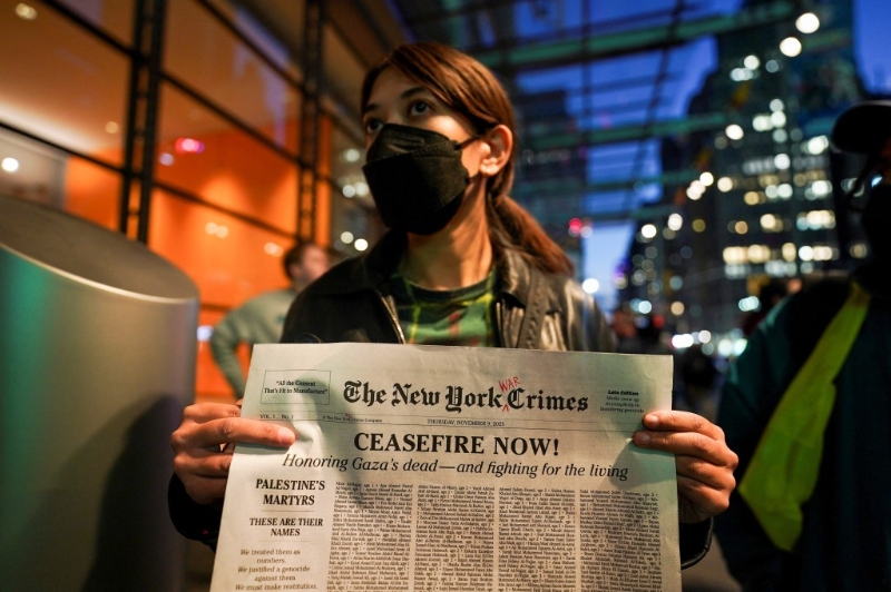 示威者高举模仿纽时封面的纸张，上面的《纽约时报》被改成《纽约战犯报》。路透社