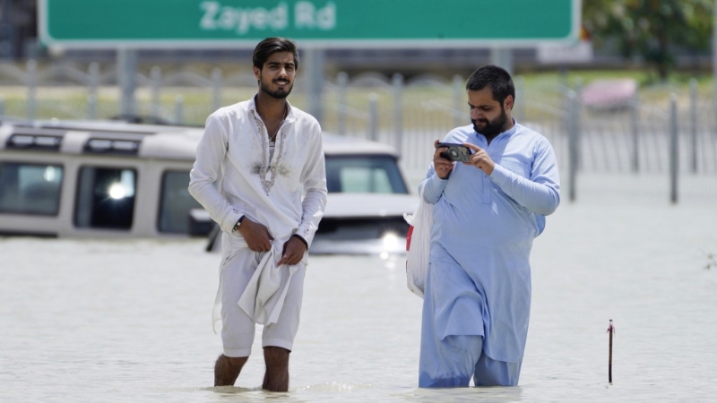 迪拜罕见暴雨，两名男子涉水而行。