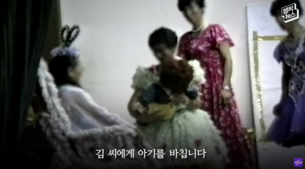 男信徒假裝孕婦，並將假娃娃獻給金己順。YouTube／Netflix Asia