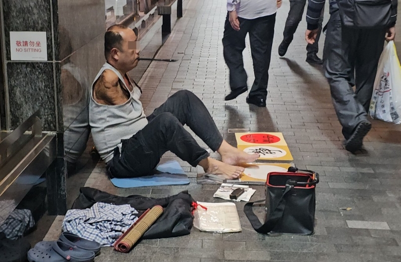 油麻地有失去双臀的行乞者口咬毛笔提字。 徐裕民摄 油麻地有失去双臀的行乞者口咬毛笔提字。 徐裕民摄
