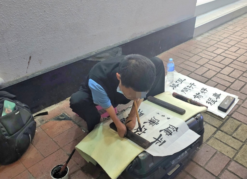 旺角有残障内地男子张口夹紧粗大毛笔写上“平安喜乐、健康是福”。 徐裕民摄 旺角有残障内地男子张口夹紧粗大毛笔写上“平安喜乐、健康是福”。 徐裕民摄