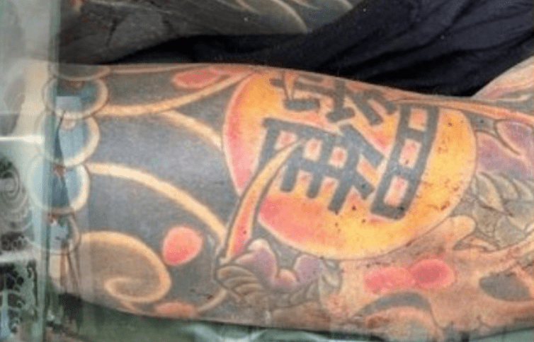 尸体上全身布满不同图案的刺青，其中手臂上刺有一个繁体的“罗”字。 泰国电视新闻截图