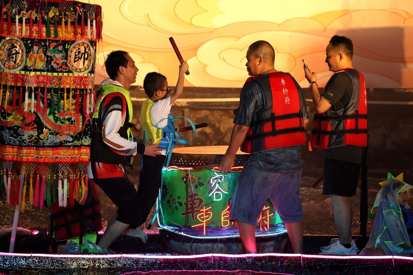 龙舟上,一位父亲抱着孩子,让他尝试击鼓 龙舟上,一位父亲抱着孩子,让他尝试击鼓