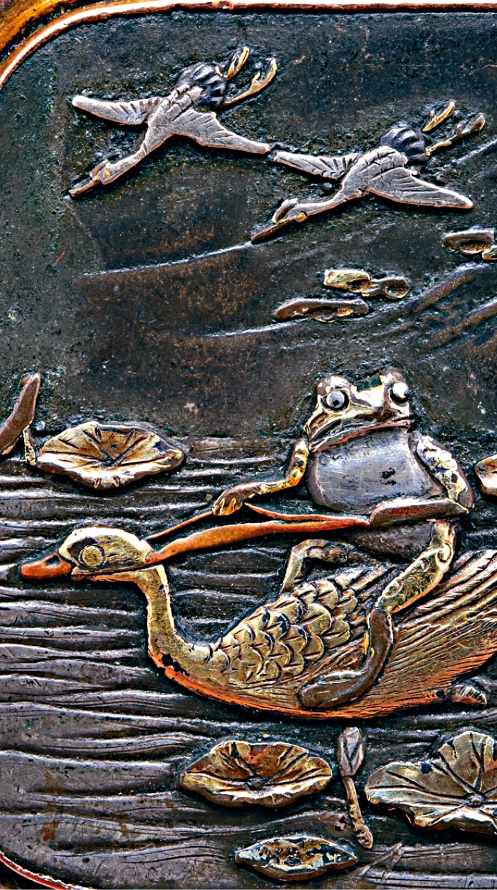 源自一枚鎏金银赤铜胸针上的图案,描绘 青蛙骑在鸭背过河。日本1800年代晚期作 品,属私人收藏。 源自一枚鎏金银赤铜胸针上的图案,描绘 青蛙骑在鸭背过河。日本1800年代晚期作 品,属私人收藏。