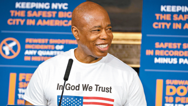 亚当斯身穿一件印有美国国旗及“我们信仰上帝”字样的T恤。 亚当斯身穿一件印有美国国旗及“我们信仰上帝”字样的T恤。