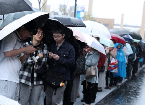 大阪世博开幕首天下大雨，民众狼狈撑伞排队入场。新华社