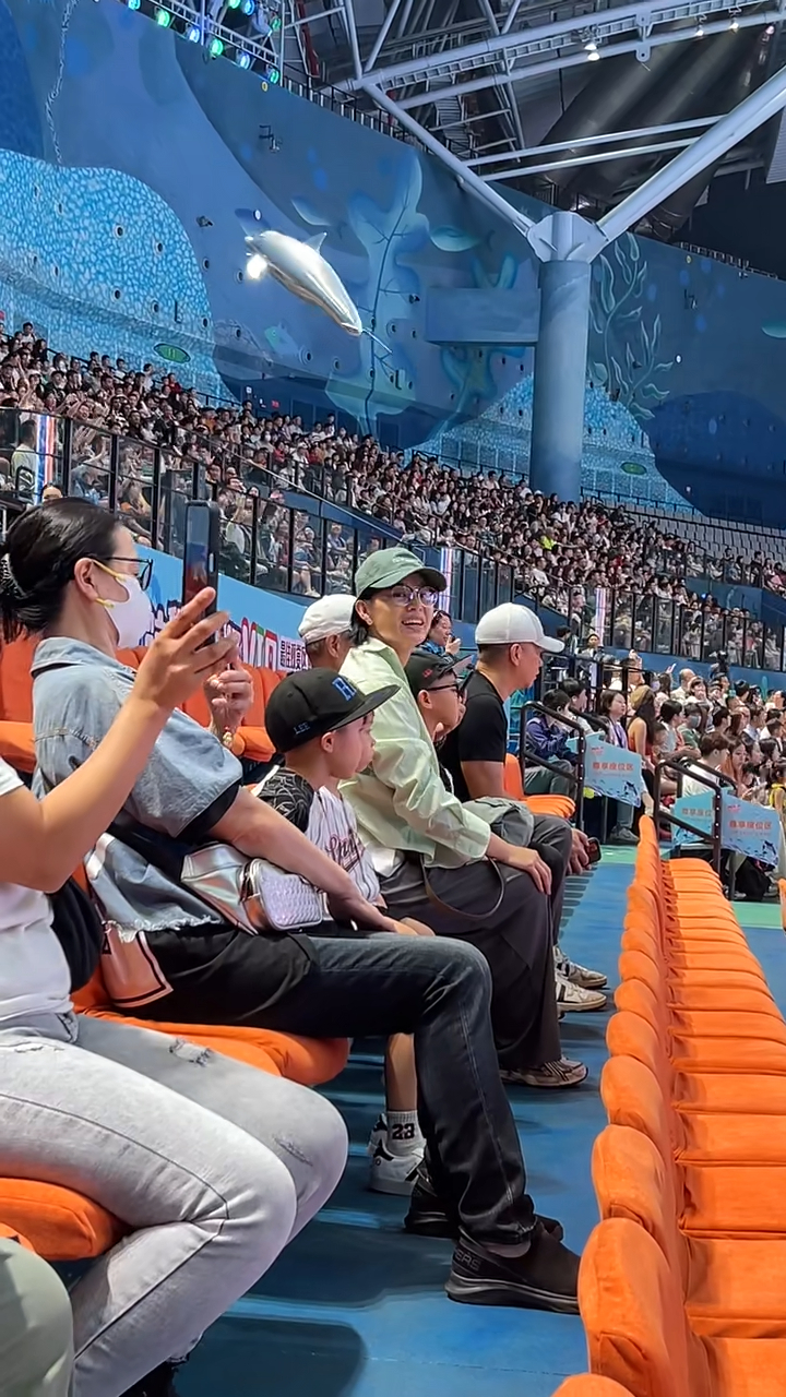 胡杏兒頭戴綠色Cap帽及身穿淺綠色襯衫，與家人一起坐在VIP區域觀看演出，她臉上掛滿笑容，時不時還揮手互動，看起來心情大好。