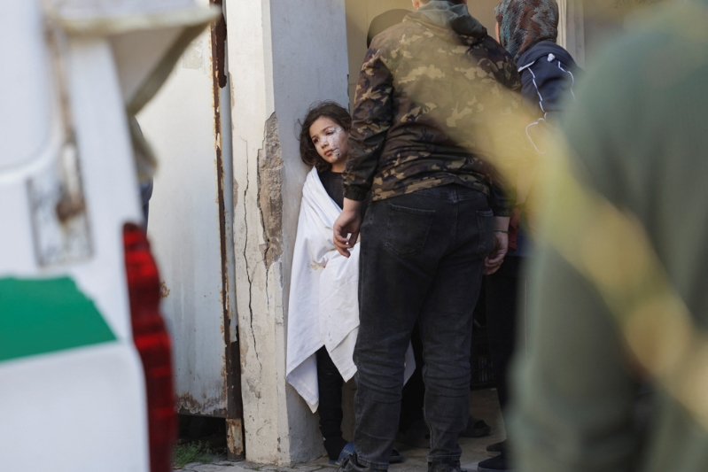 一名满脸是伤的女孩目睹救护员把她已身亡的父亲抬上车准备送去下葬的场面，神色茫然。